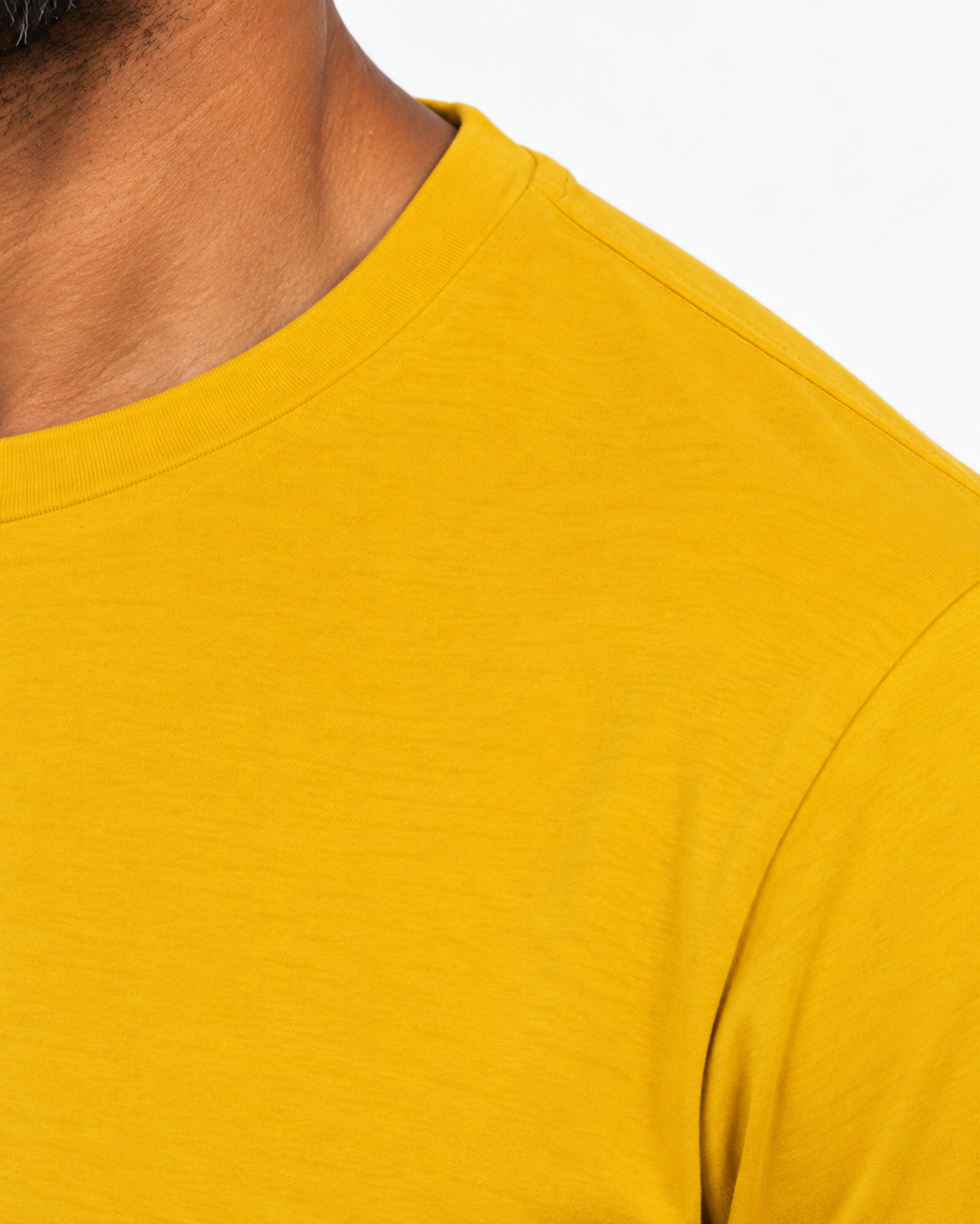 Detalhe lateral da gola e costura do ombro da camiseta amarela.